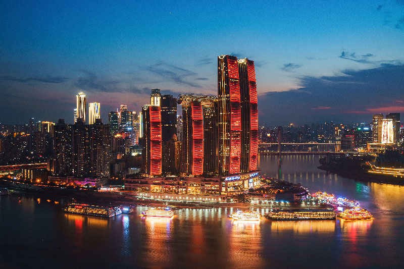 Espectacular vista panorámica nocturna del skyline iluminado de Chongqing y barcos turísticos en el río.