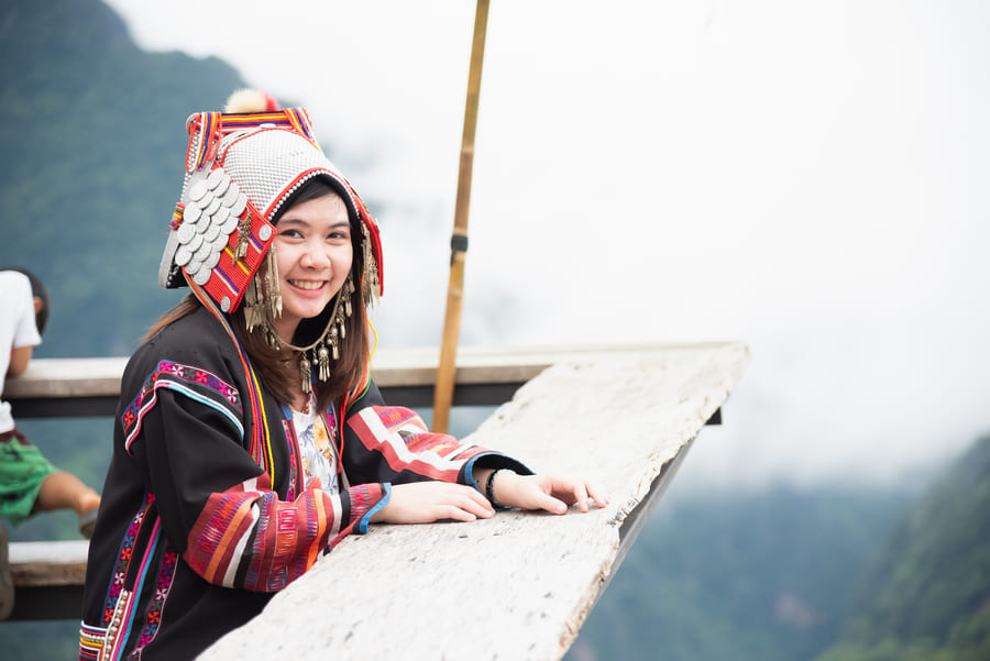 Joven sonriente con traje y tocado tradicional Akha en un mirador de madera en Yunnan, China